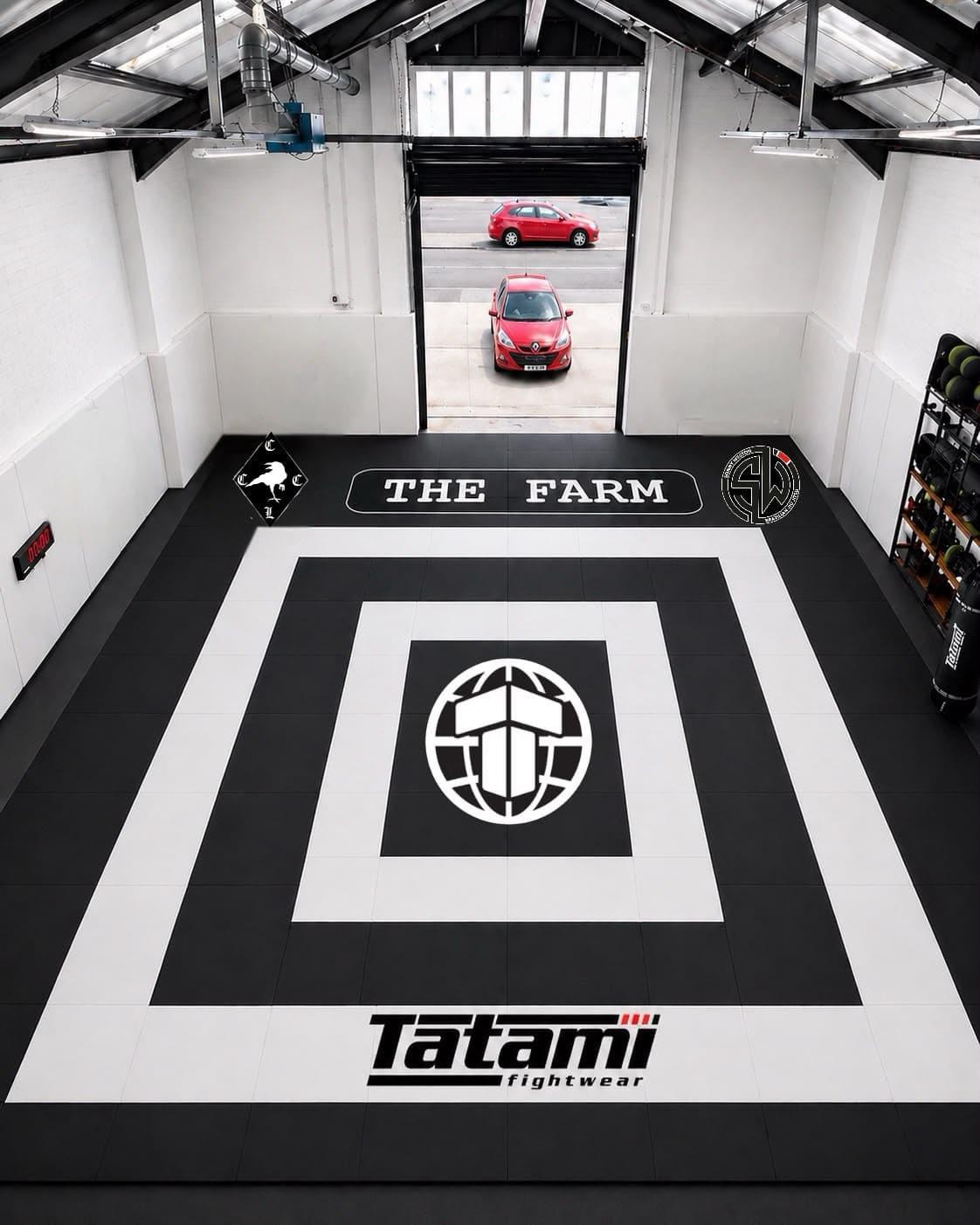 The competition mat from above: a black diamond on white tatami with the SWBJJ emblem in the centre and The Farm sign on the wall