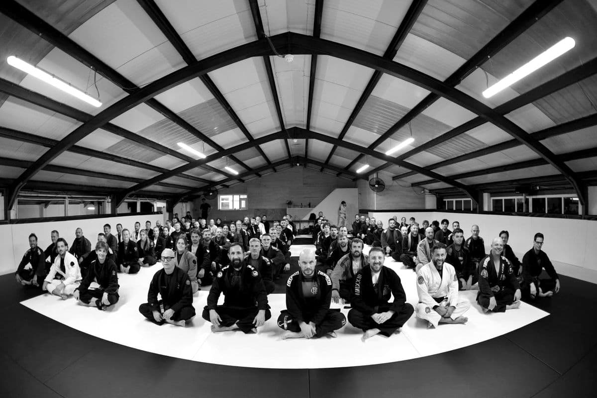 The whole SWBJJ adults team seated on the mat under the roof of the new academy, black and white